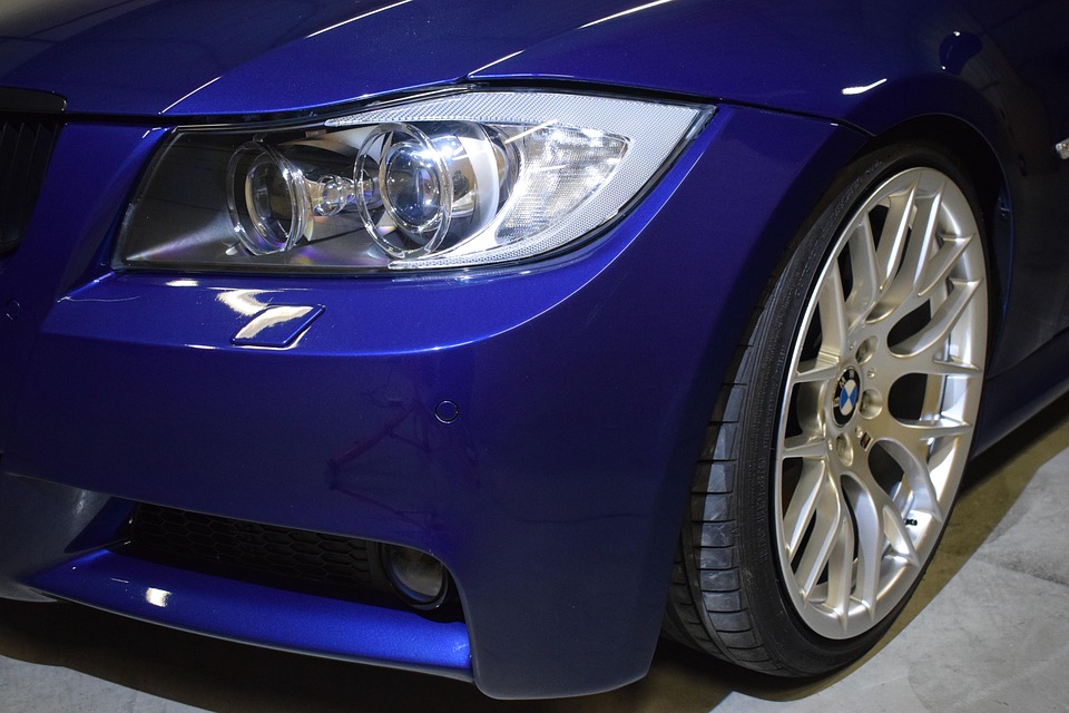 Detailaufnahme eines blauen BMW mit glänzendem Scheinwerfer und silberner Felge